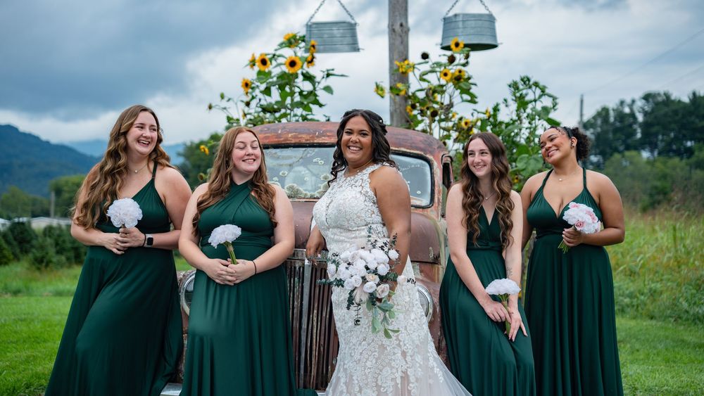 Wedding party in emerald green dresses poses together in a scenic mountain meadow during summer celebration.