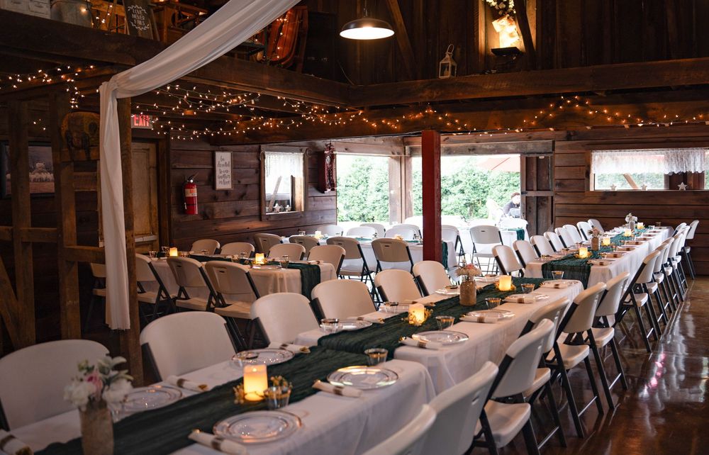 Long banquet tables decorated with white linens and twinkle lights in a rustic wooden reception venue.