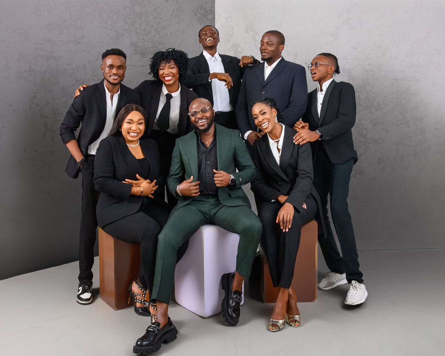 A group of stylishly dressed people in business attire pose together against a gray studio backdrop.