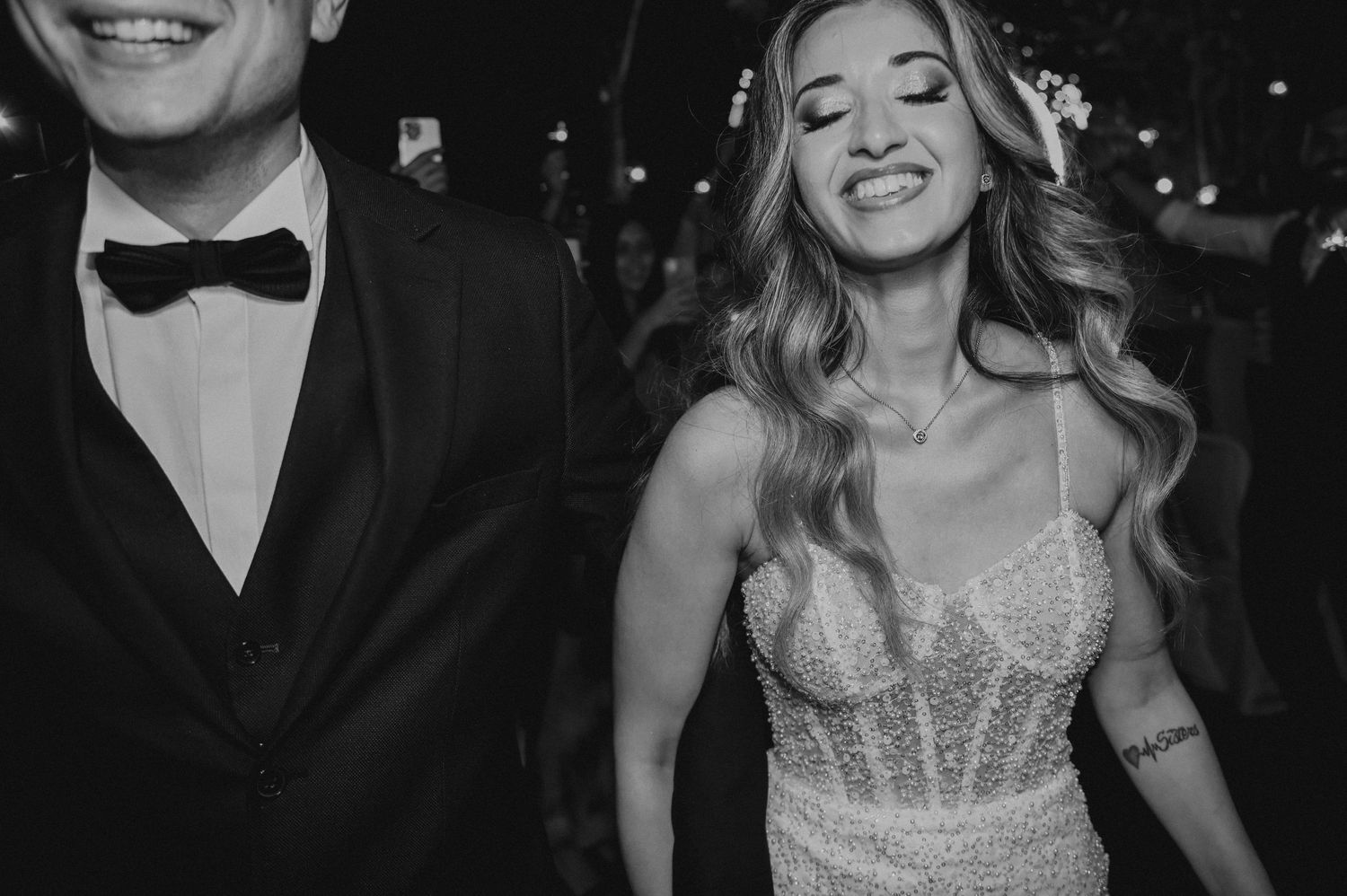 A black and white candid photo of a bride in a strapless gown laughing joyfully next to someone in a tuxedo.