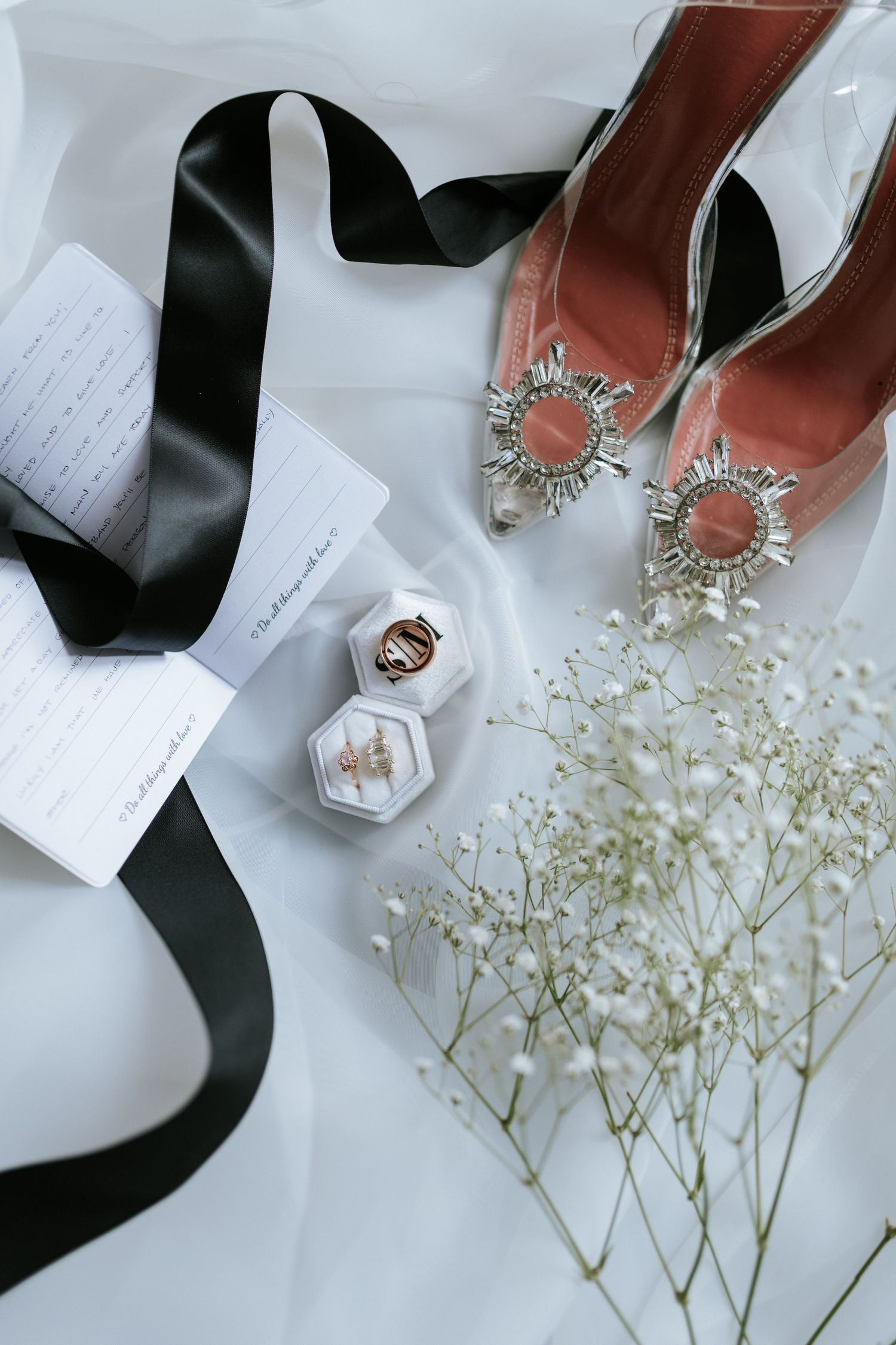 Wedding accessories including black ribbon, pink heels with crystal embellishments, and baby's breath flowers.