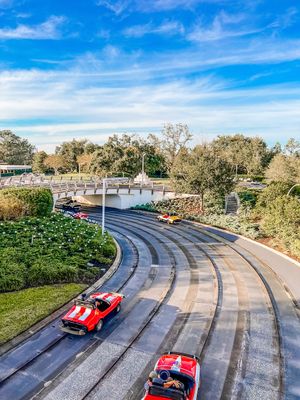 Red cars navigate a winding track at Tomorrowland Speedway in Disney's Magic Kingdom theme park on a sunny day.
