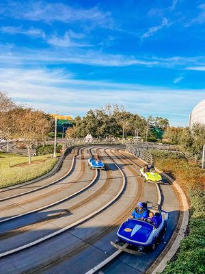 Alpine slide riders glide down a curved track through autumn scenery under bright blue skies.