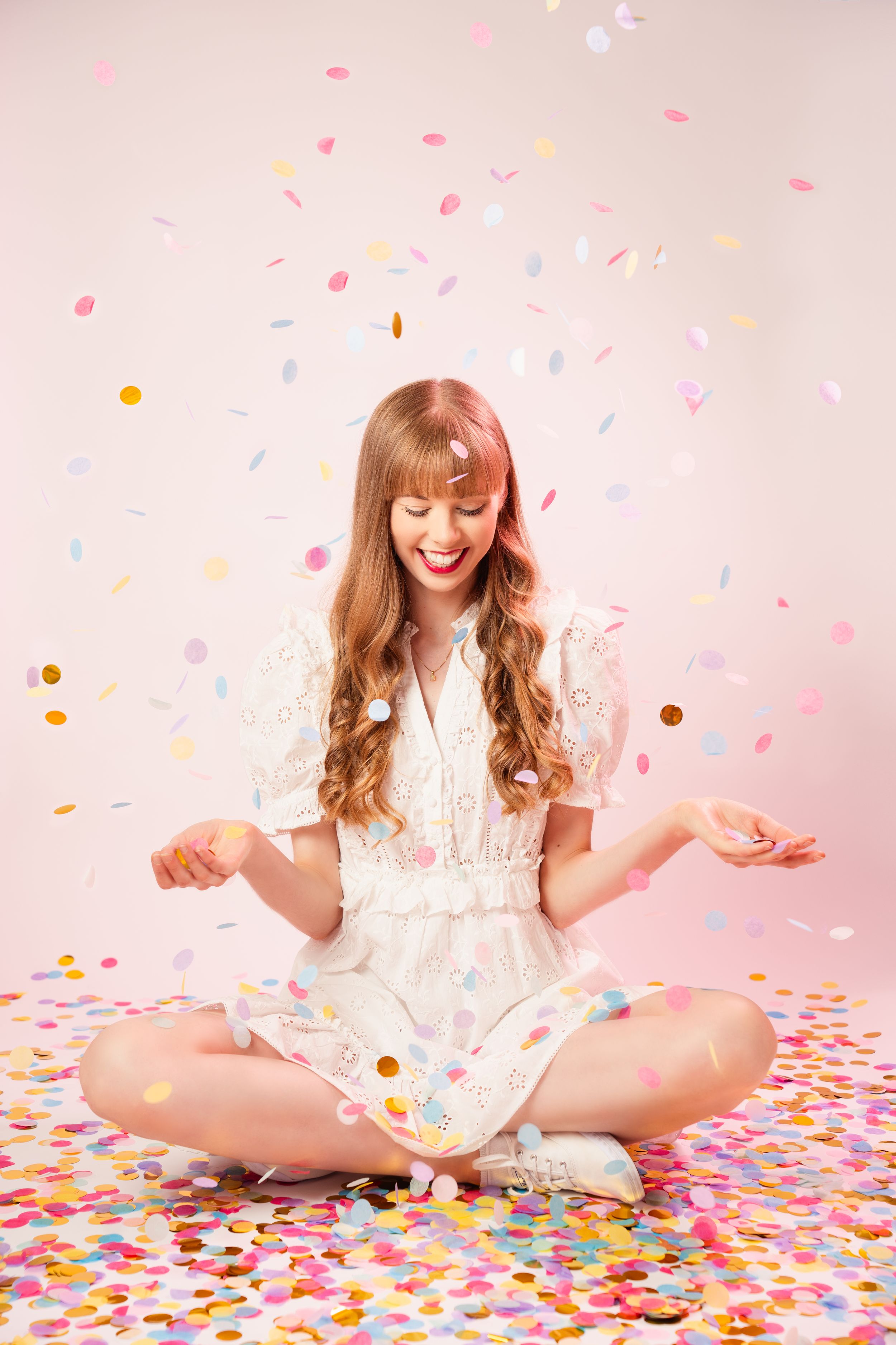 A carefree moment captured with falling confetti and a white dress against a pink backdrop. Wedding celebrant photography.