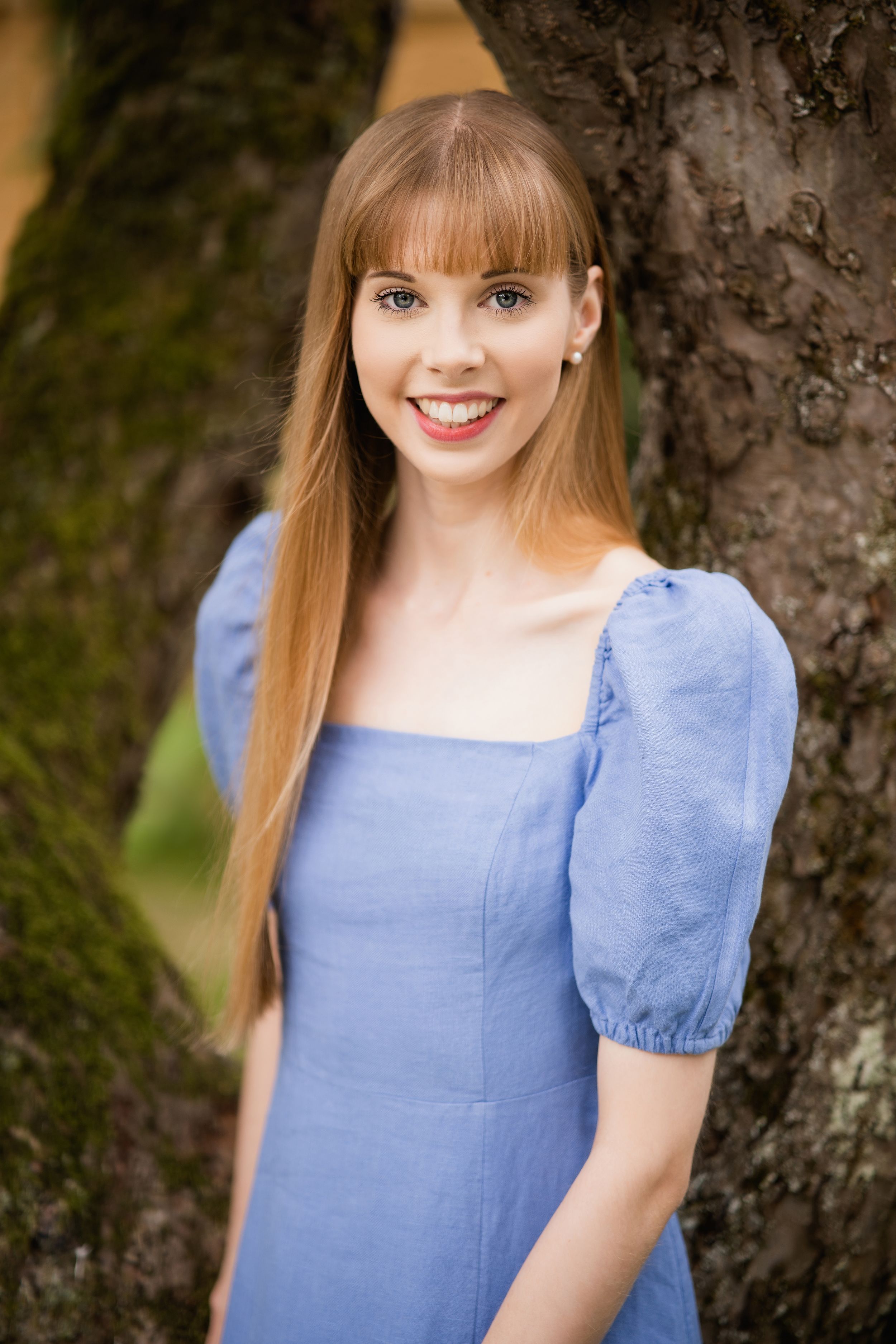 Someone in a blue puff-sleeve dress stands next to a tree trunk in a natural outdoor setting. Personal Branding Photography Surrey.