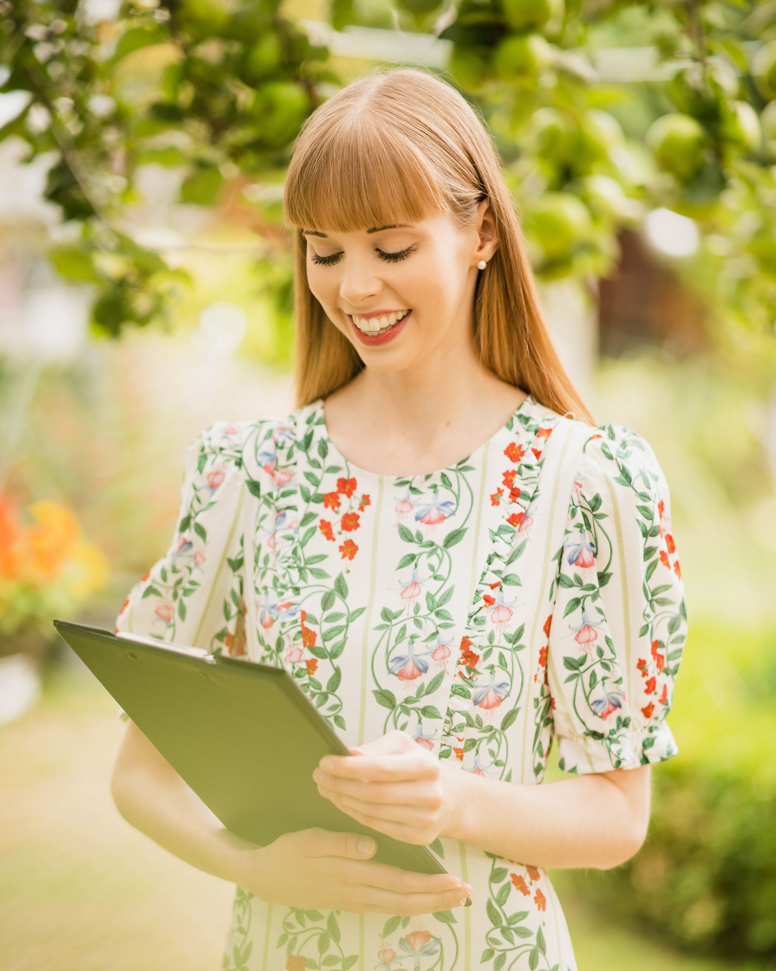 Reading from a folder while wearing a floral dress in a sunny garden setting. Personal Branding Photography Surrey.