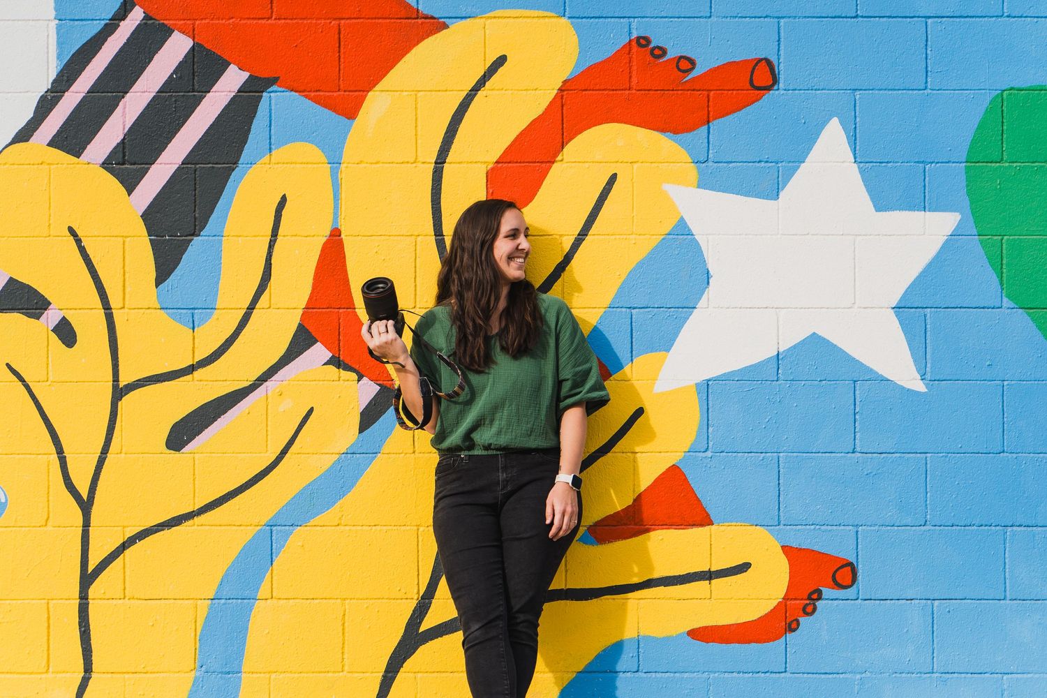 Person standing against colorful mural wall with yellow shapes and white stars.