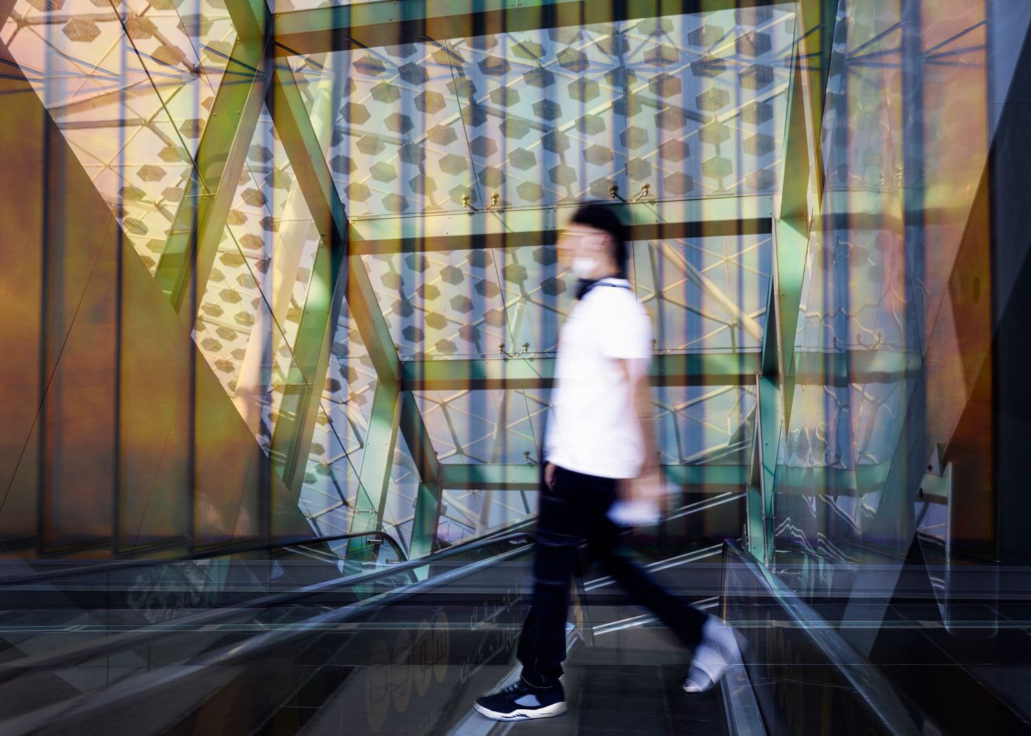 Motion blur of person walking through modern corridor with geometric reflective walls and green accents in urban setting.