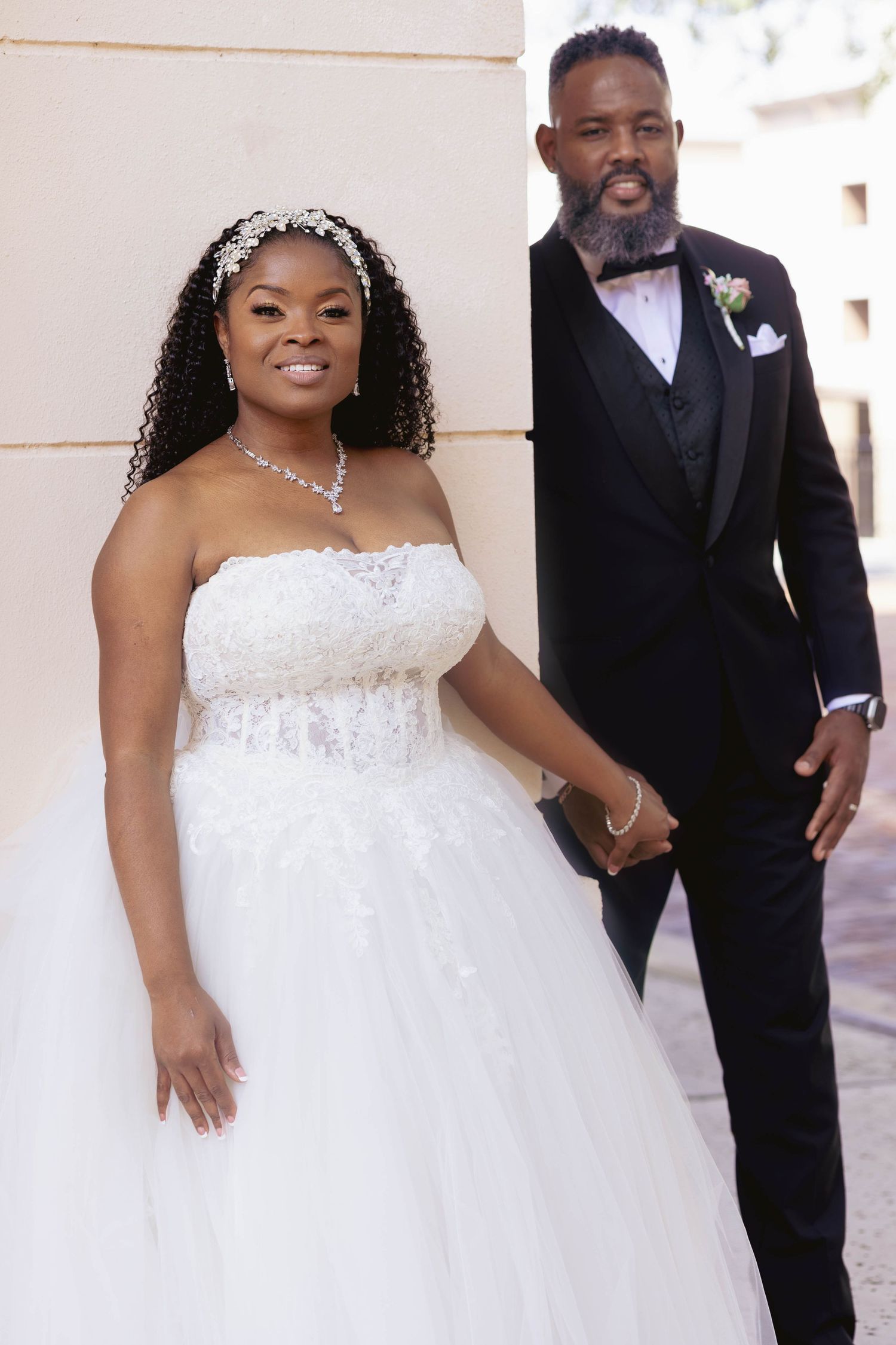 A bride in a white strapless ballgown and groom in a black tuxedo pose elegantly for their wedding portrait.