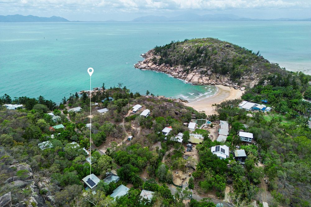 Aerial view of a tropical coastline with turquoise waters, green vegetation, and scattered buildings along the shore.