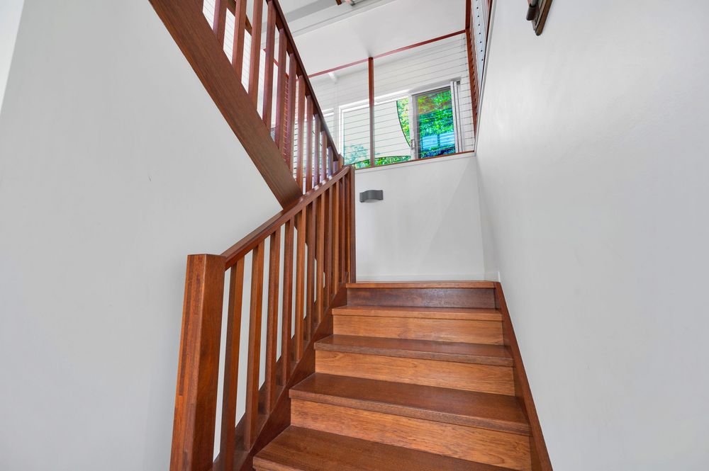 Wooden staircase with warm brown handrails and white walls leads upwards in a residential interior.
