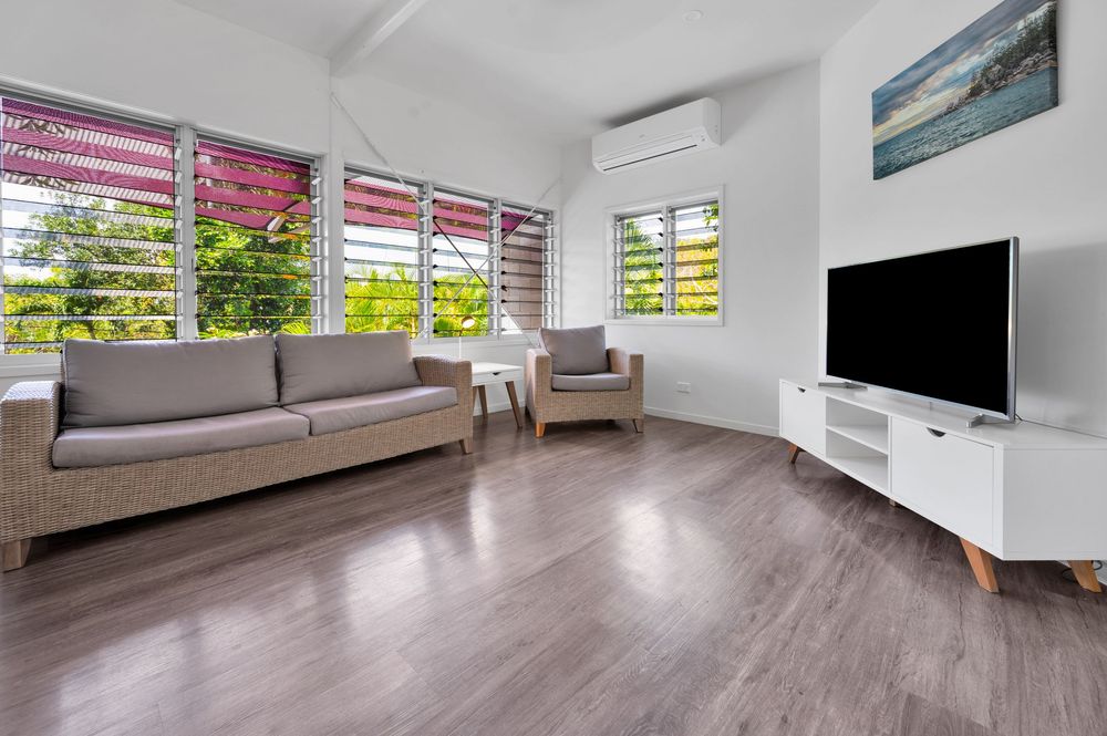 Modern apartment interior with louvered windows, air conditioning unit, and wood flooring in bright natural light.
