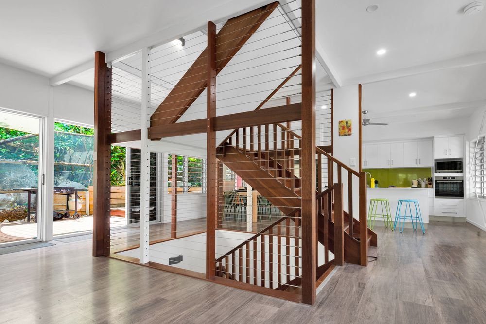 Modern open concept living area with wooden staircase, white walls, and hardwood floors showcasing natural light and clean lines.