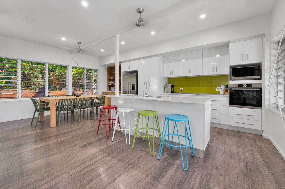 Modern open kitchen with colorful bar stools, white countertops, and wooden dining table in an open-concept space.