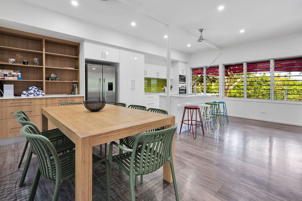Modern open concept kitchen and living space with recessed lighting, hardwood floors, and green accent chairs.