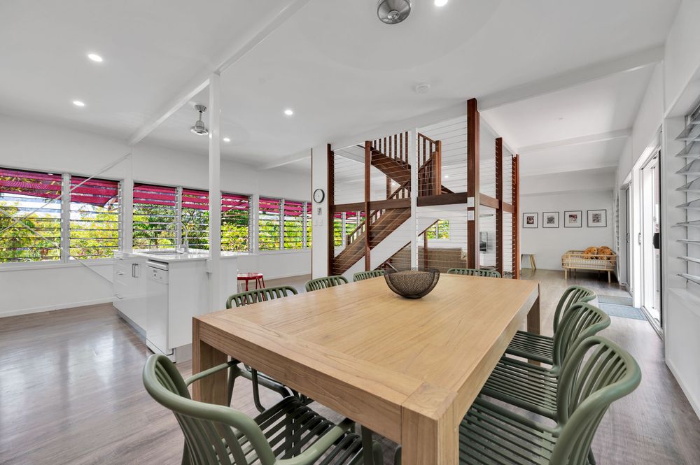 Modern open concept living space features white walls, wood floors, and natural light streaming through large windows.