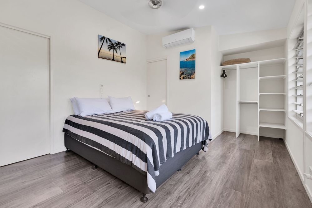 Minimalist bedroom featuring gray wood floors, white walls, and striped bedding in contemporary design.
