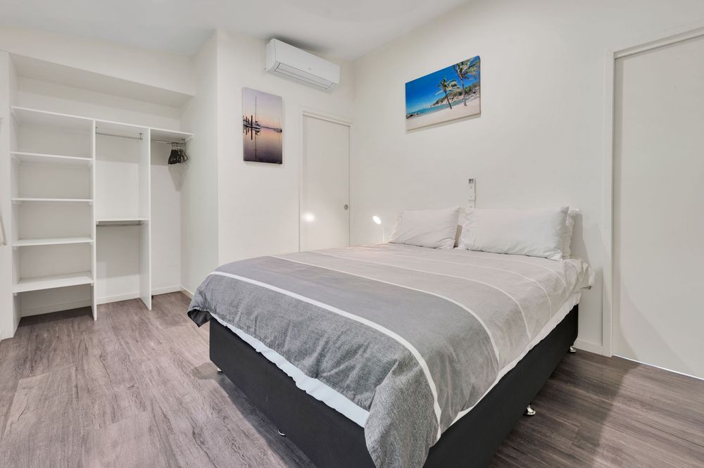 Contemporary bedroom with grey bedding, built-in shelving, and hardwood floors featuring coastal artwork.