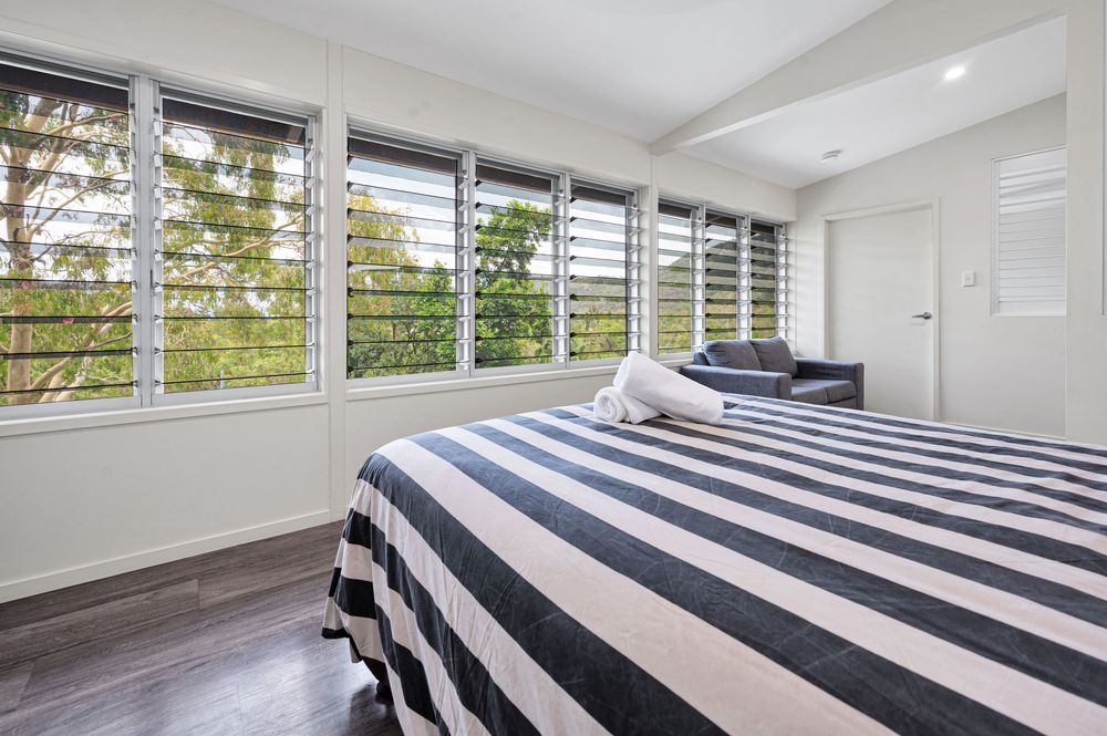Modern bedroom interior with white shutters and striped black and white bedding in natural light.