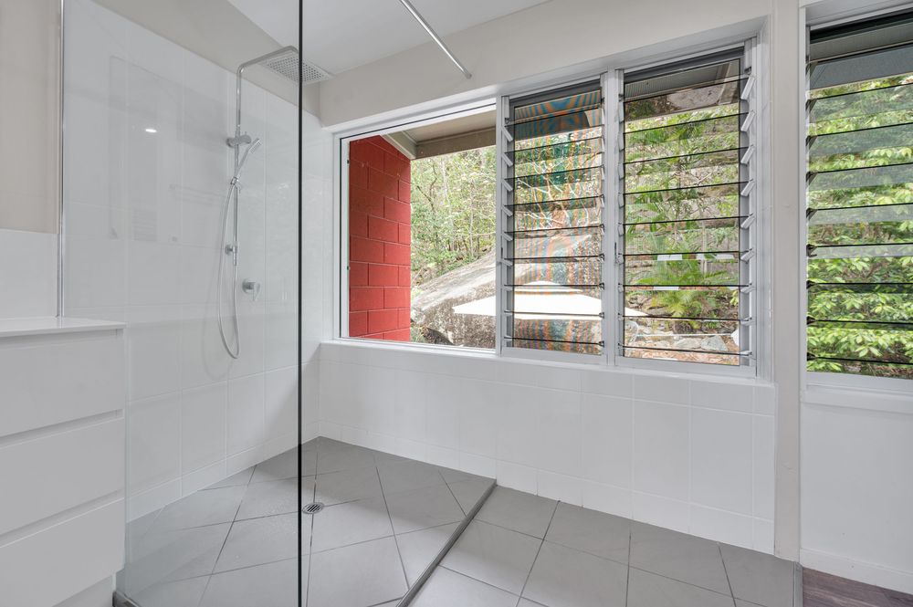 Bright white bedroom with louvered windows and natural light streaming in features minimalist architectural details.
