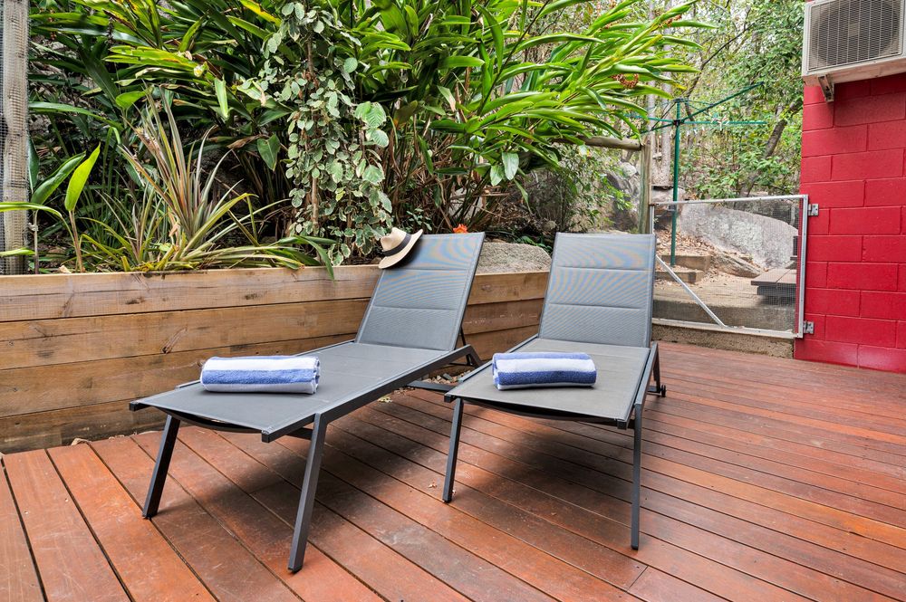 Modern outdoor wooden deck with lounge chairs and tropical plants creating a relaxing backyard oasis.