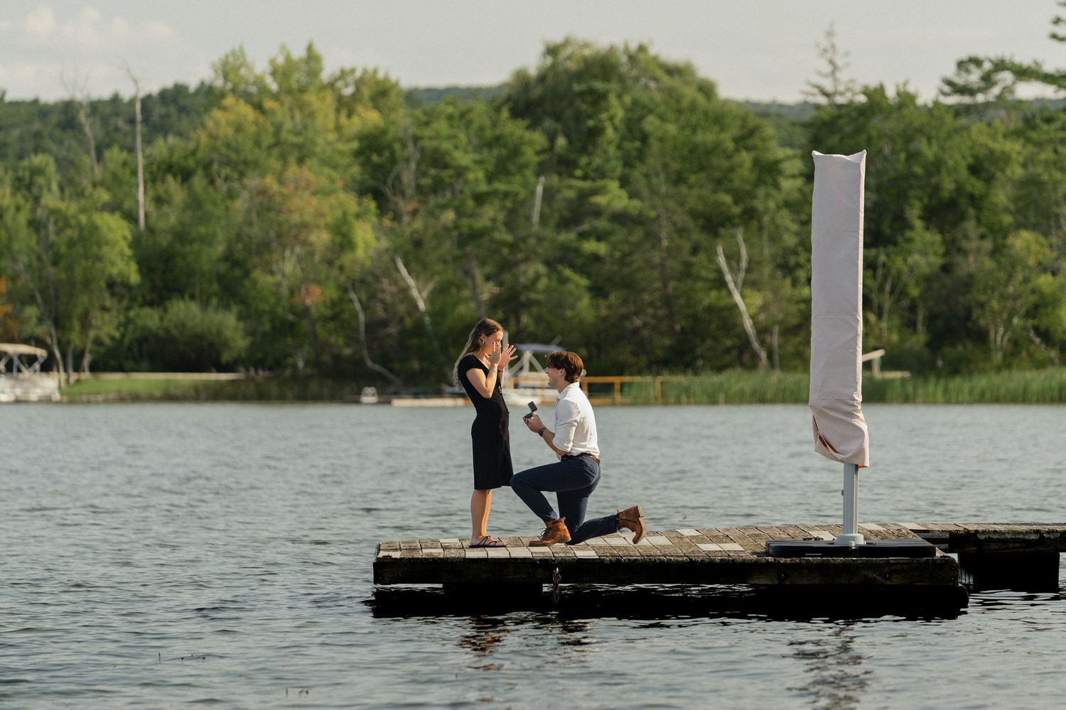 A romantic marriage proposal taking place on a wooden dock over a serene lake.