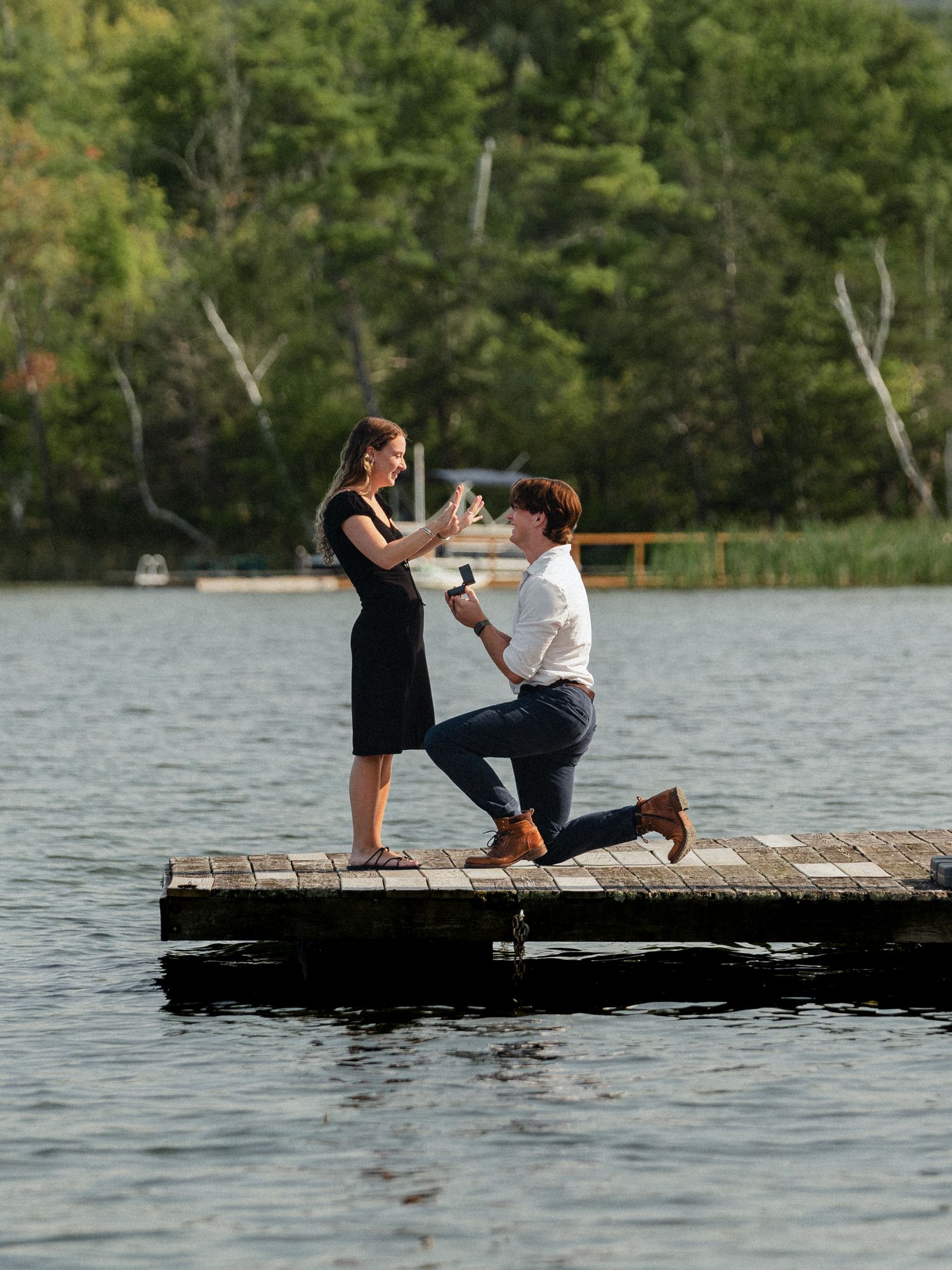 A couple sharing a special moment during a proposal on a dock by the lake.