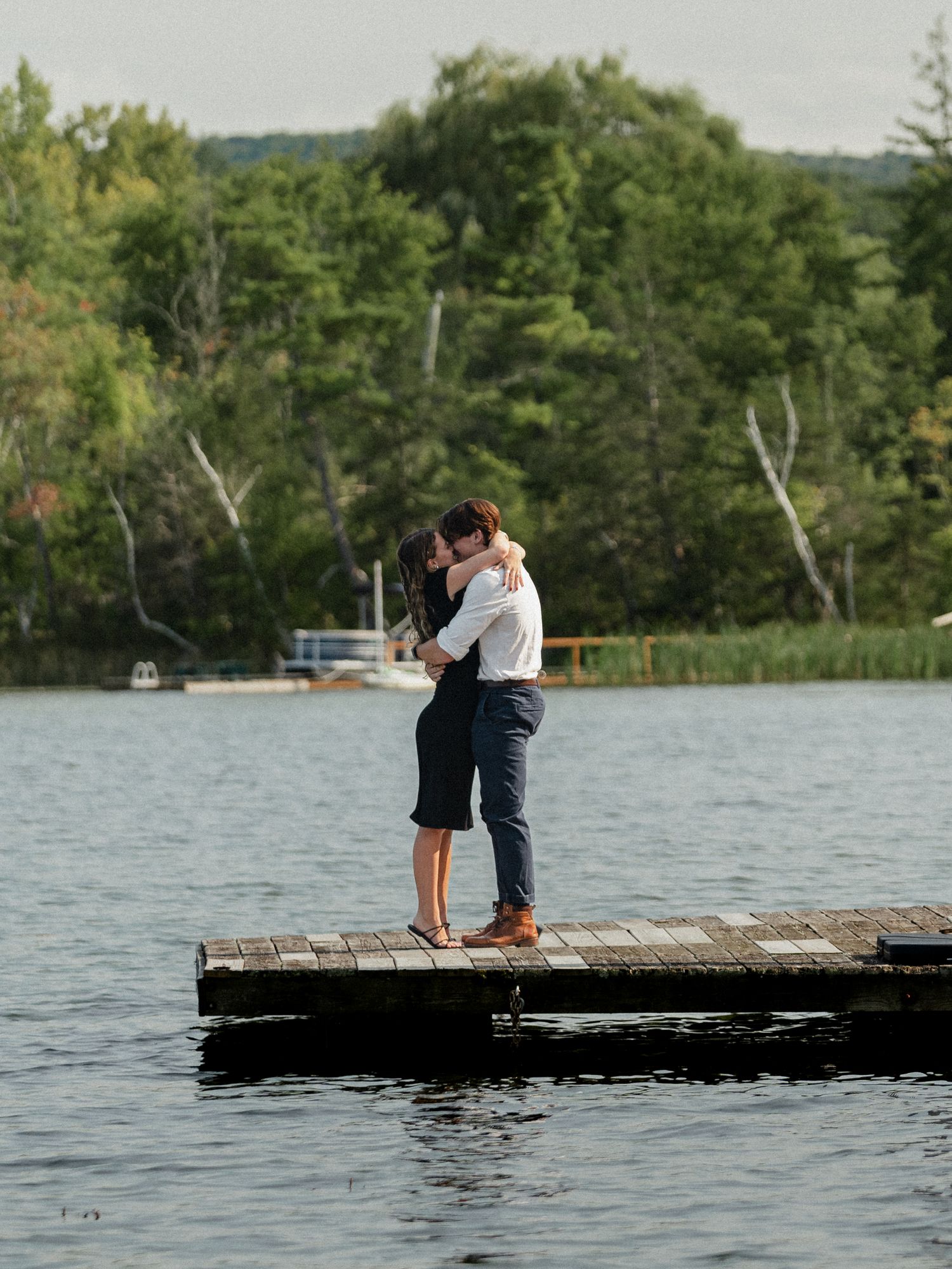 A couple embracing on a wooden dock surrounded by calm waters and forest scenery.