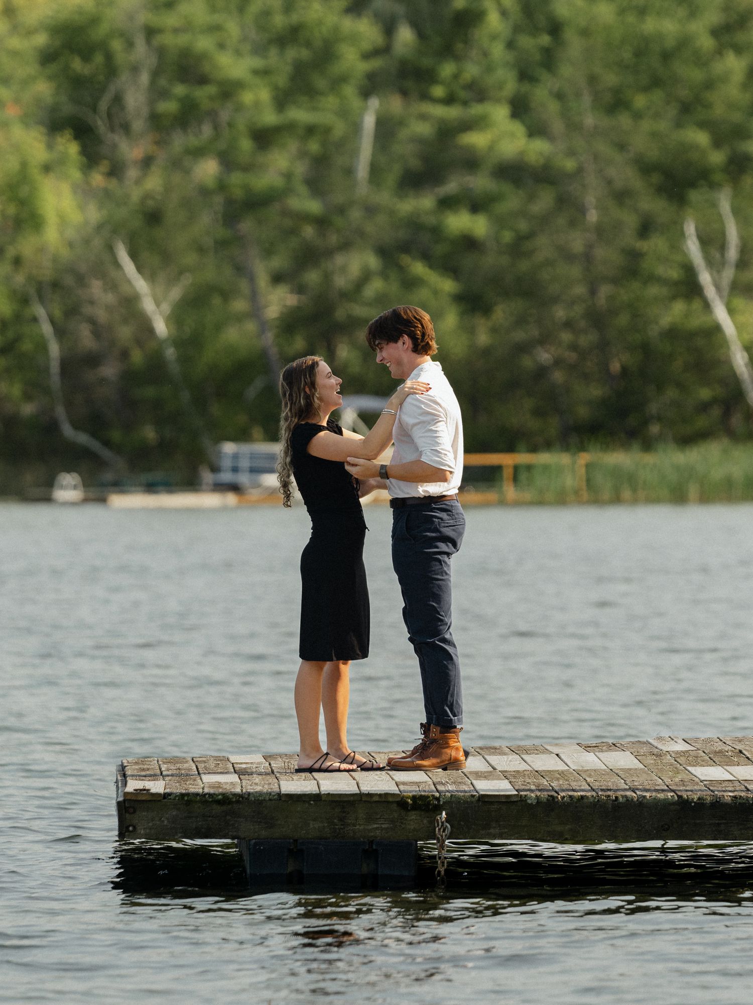 A couple shares an intimate moment while standing on a wooden dock overlooking a peaceful lake.