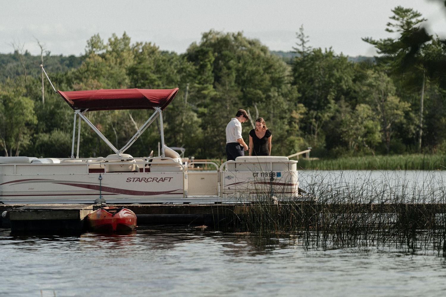 A couple enjoys a romantic moment on a pontoon boat docked at a peaceful lake.