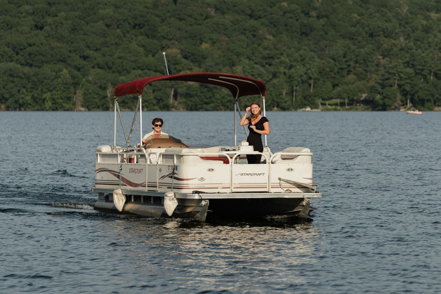 Pontoon boats cruising on a tranquil lake surrounded by green hills on a sunny day.