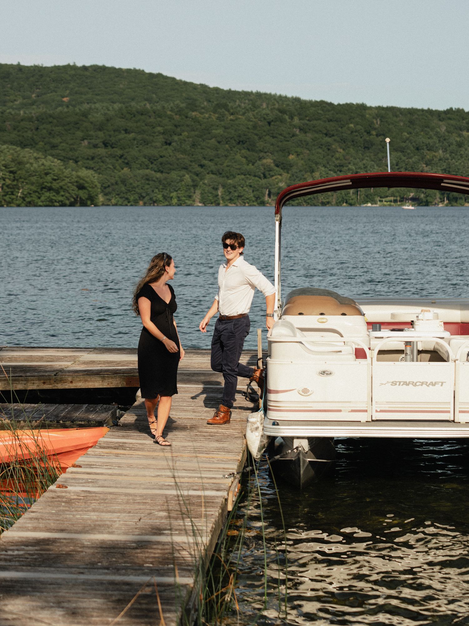 People walking along a wooden dock next to a pontoon boat on a sunny lake day.