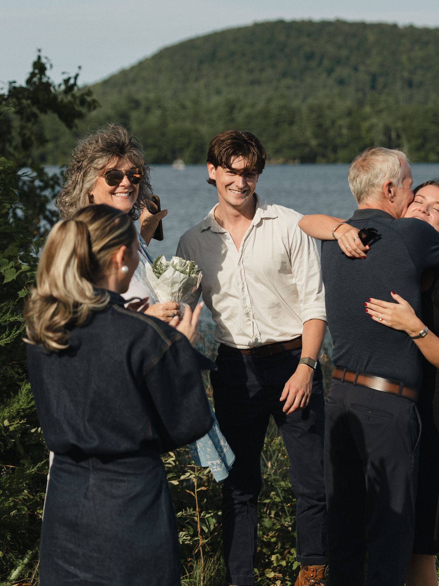 Group hugging and sharing emotional moments by the lakeside during golden hour.