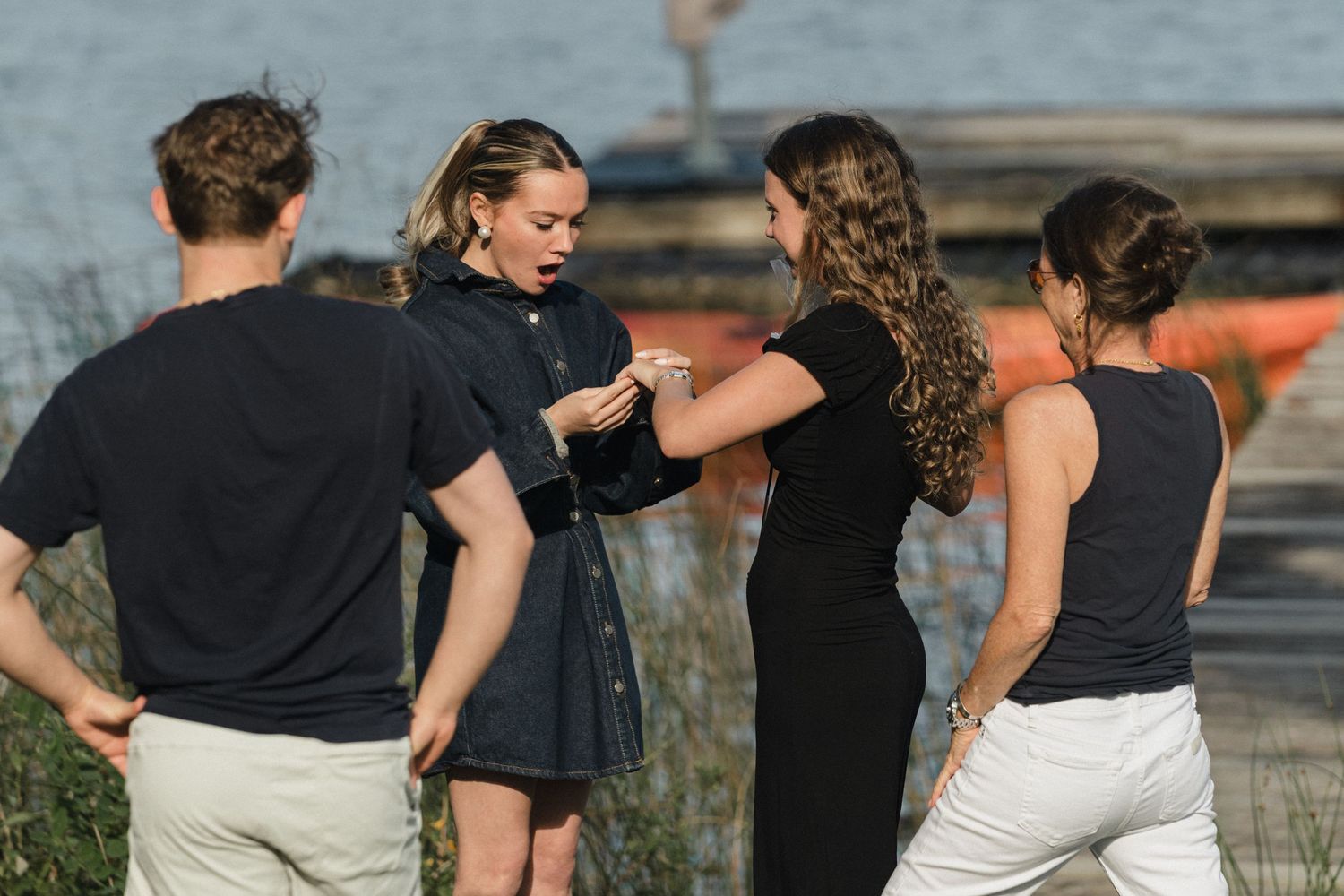 People gathered outdoors sharing emotional hugs and embraces near a lake.