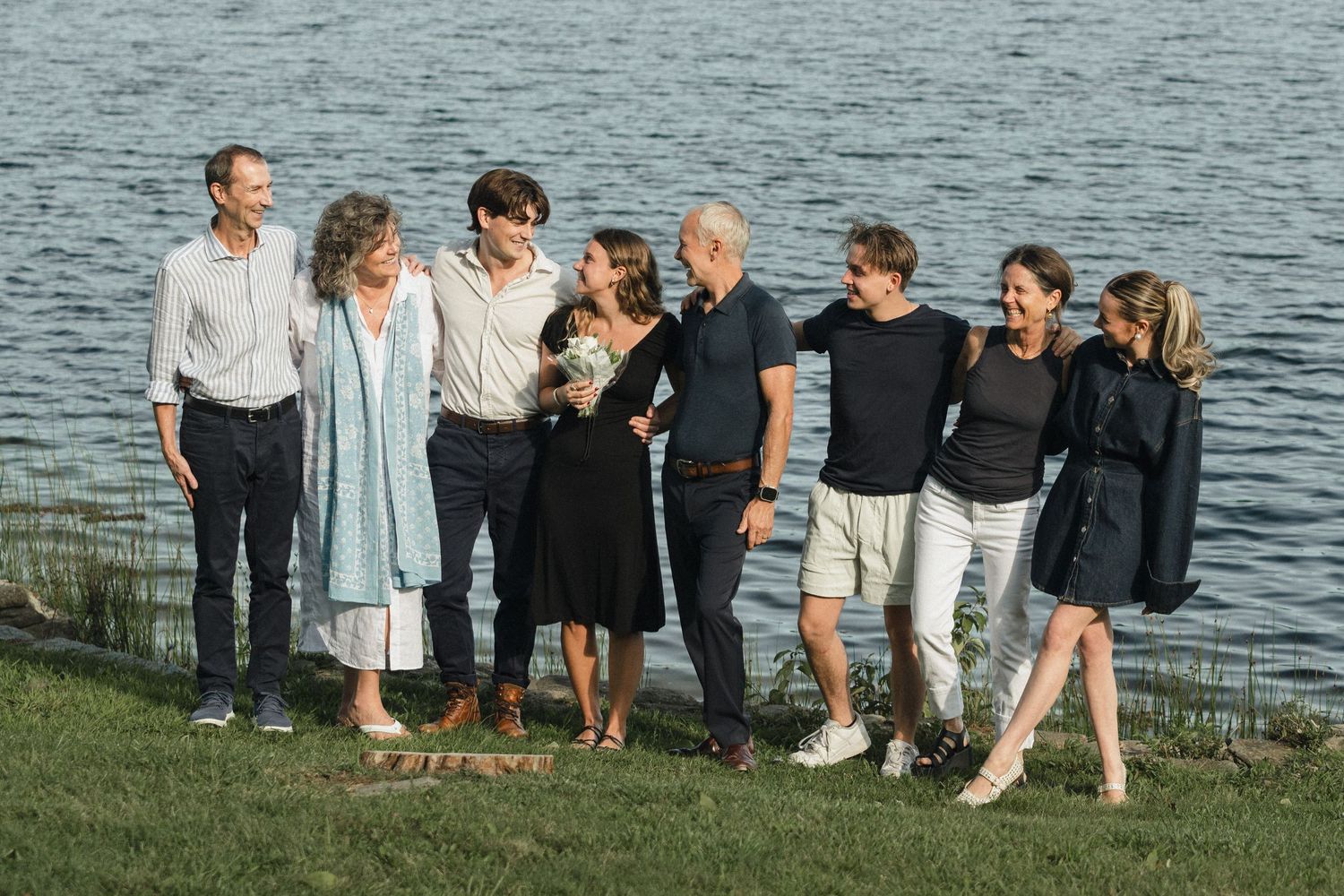Group sitting together on grass by lake during outdoor gathering.