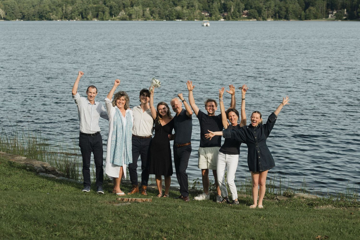 Group posing together with raised arms in celebration by waterfront.