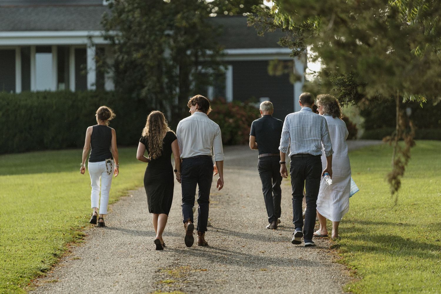 Group walking along gravel driveway with house in background.