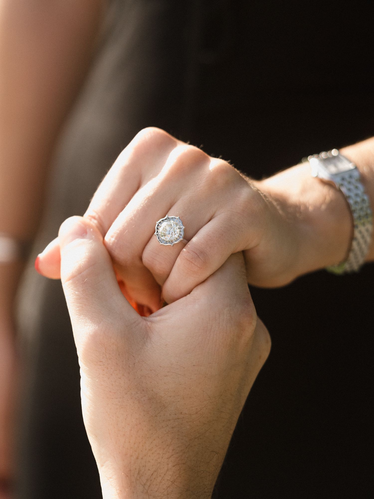 Close-up of hands holding each other, showcasing an elegant engagement ring with a silver band.