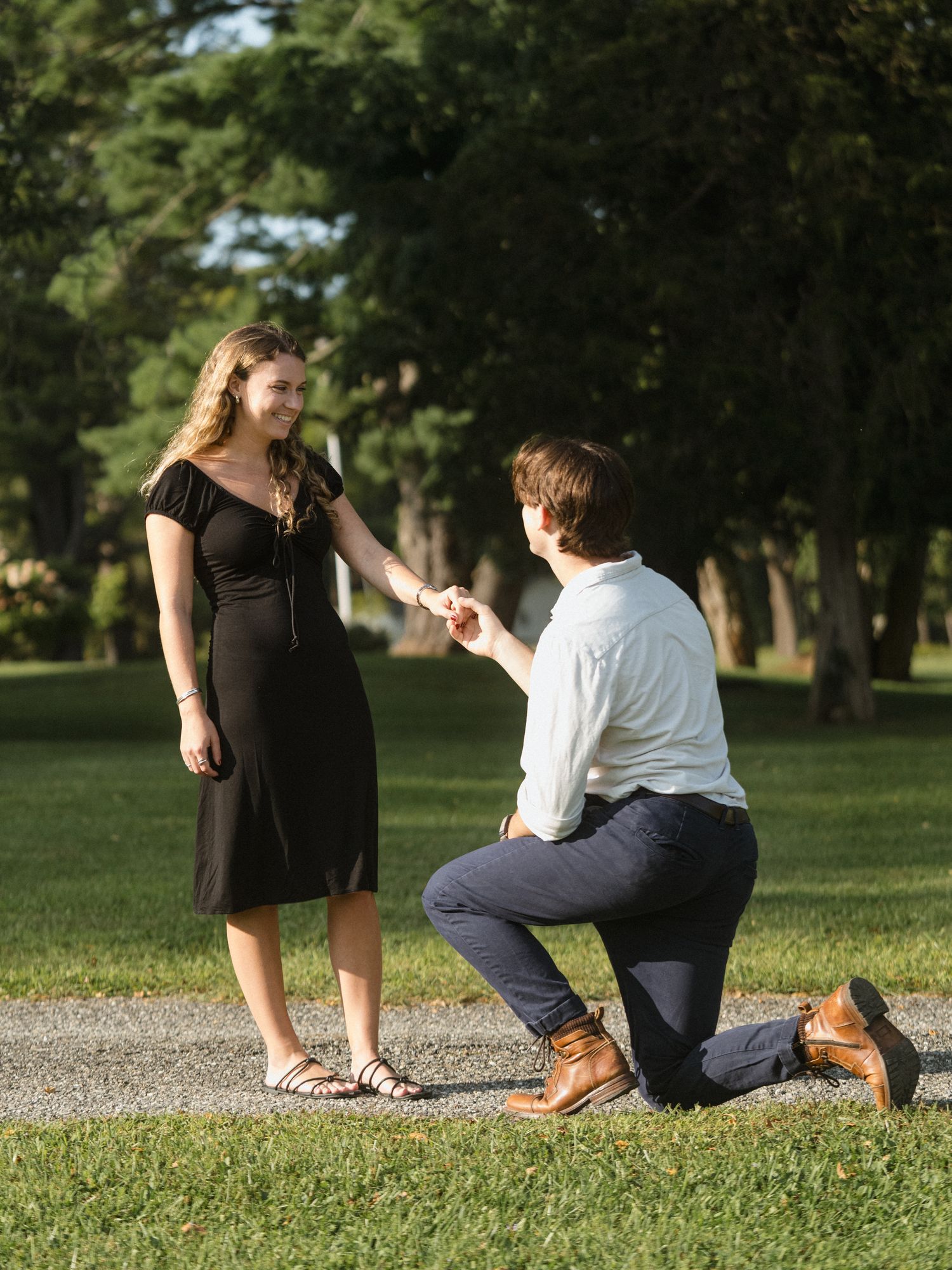 Couple sitting together on grass near a gravel path in a sunny park setting.