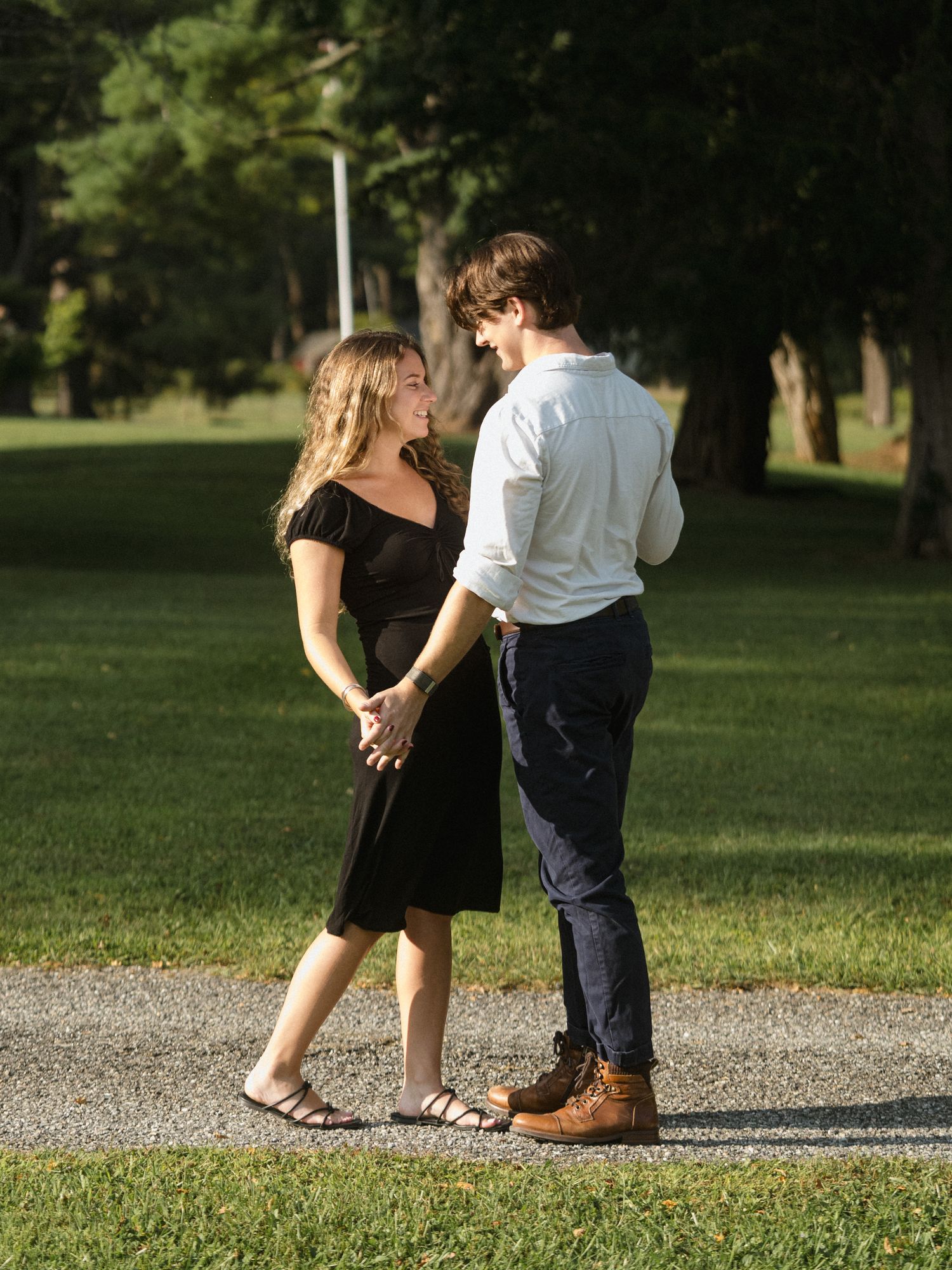 Couple walking hand in hand along a gravel path through a green park.