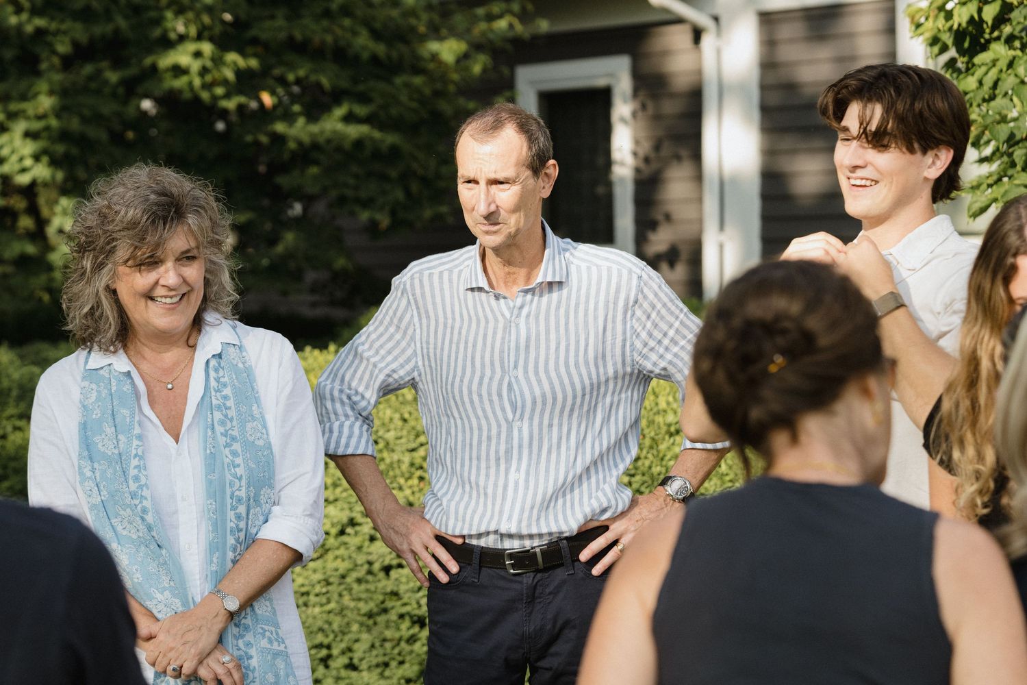 A small group gathers outdoors in front of a house during a sunny day.