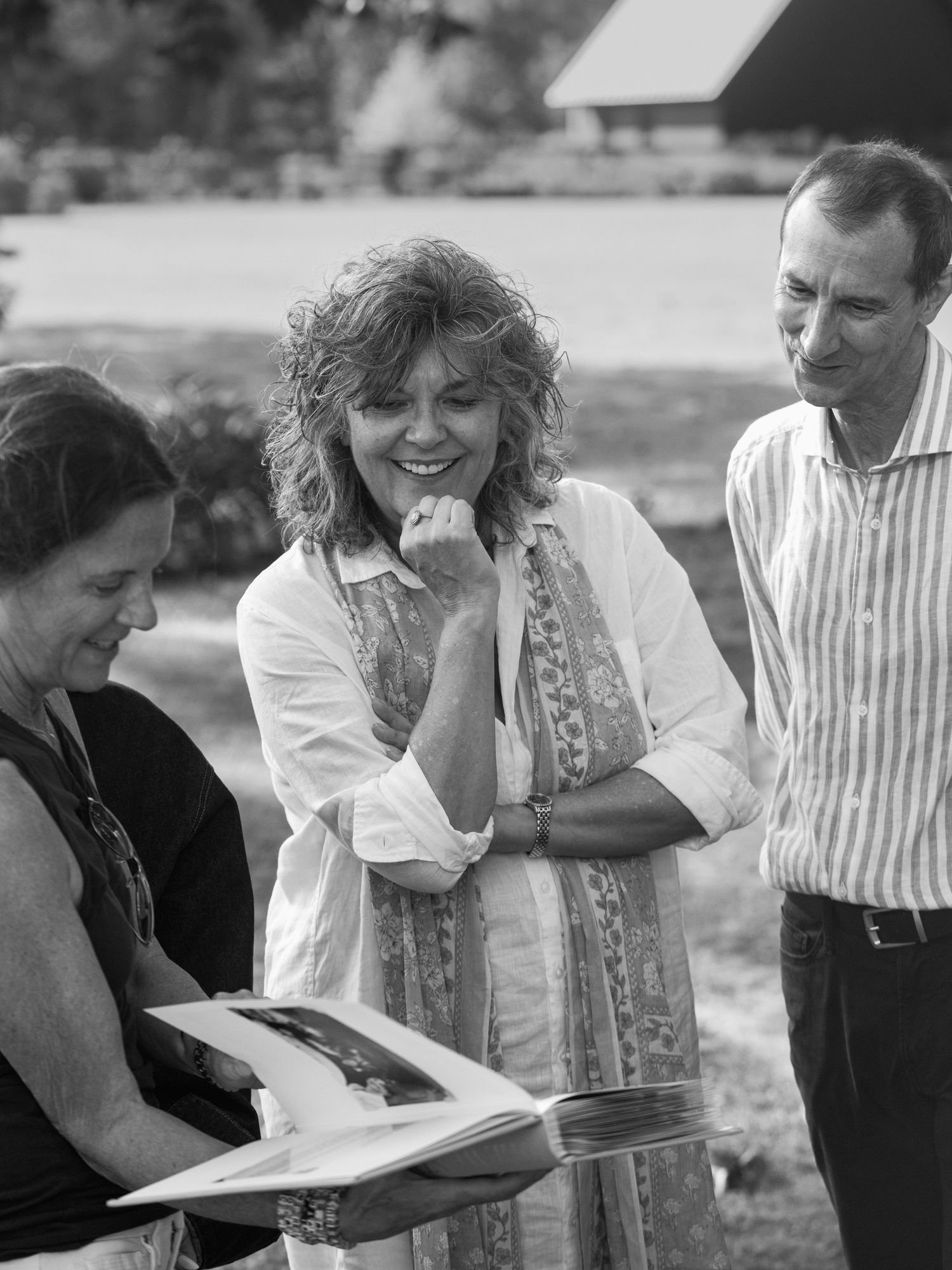A black and white photo of three people looking at a document together outdoors.