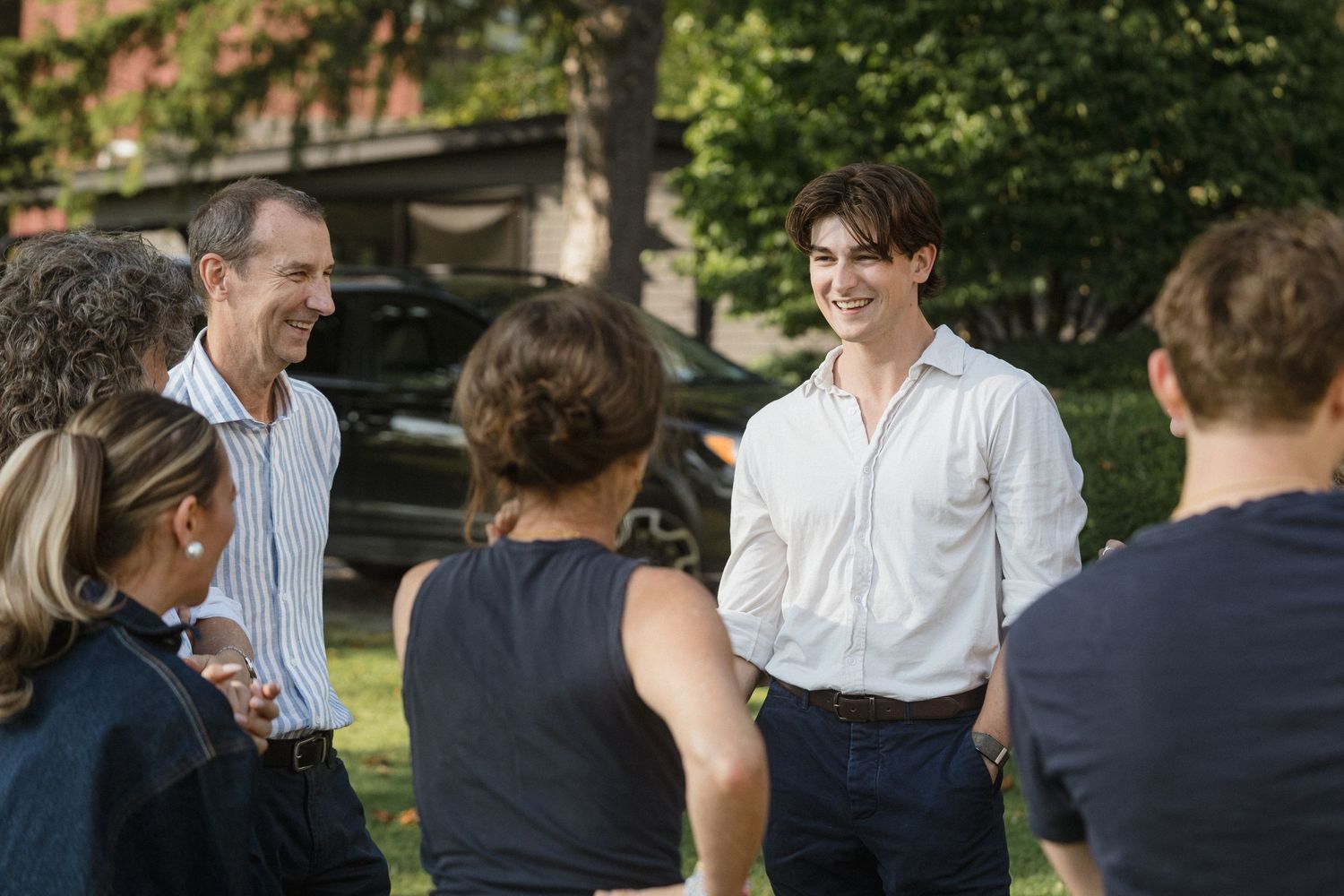 A small group gathers for conversation on a sunny lawn with trees in the background.