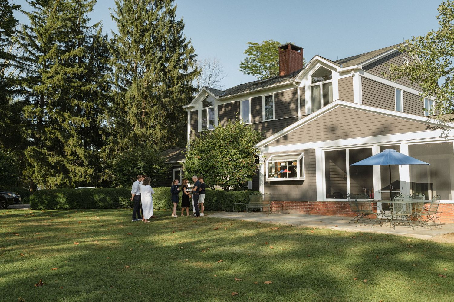 A large modern house with people gathered on the lawn for an outdoor event.