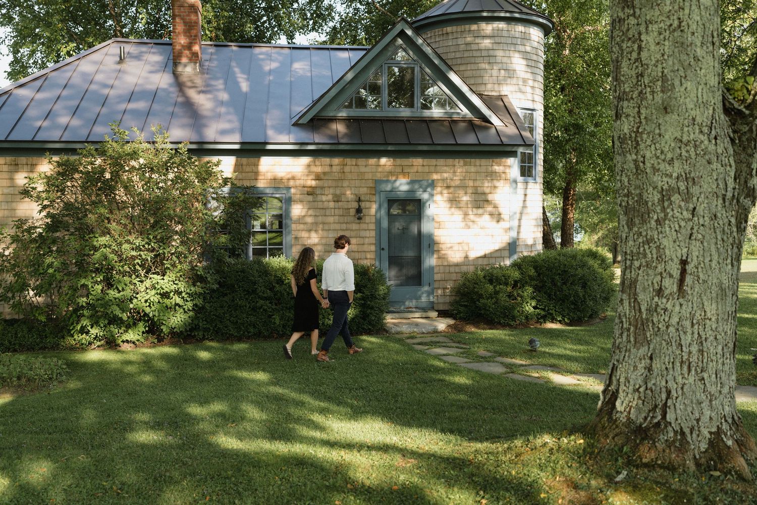 Two people walking near a charming stone cottage with a glass roof feature.