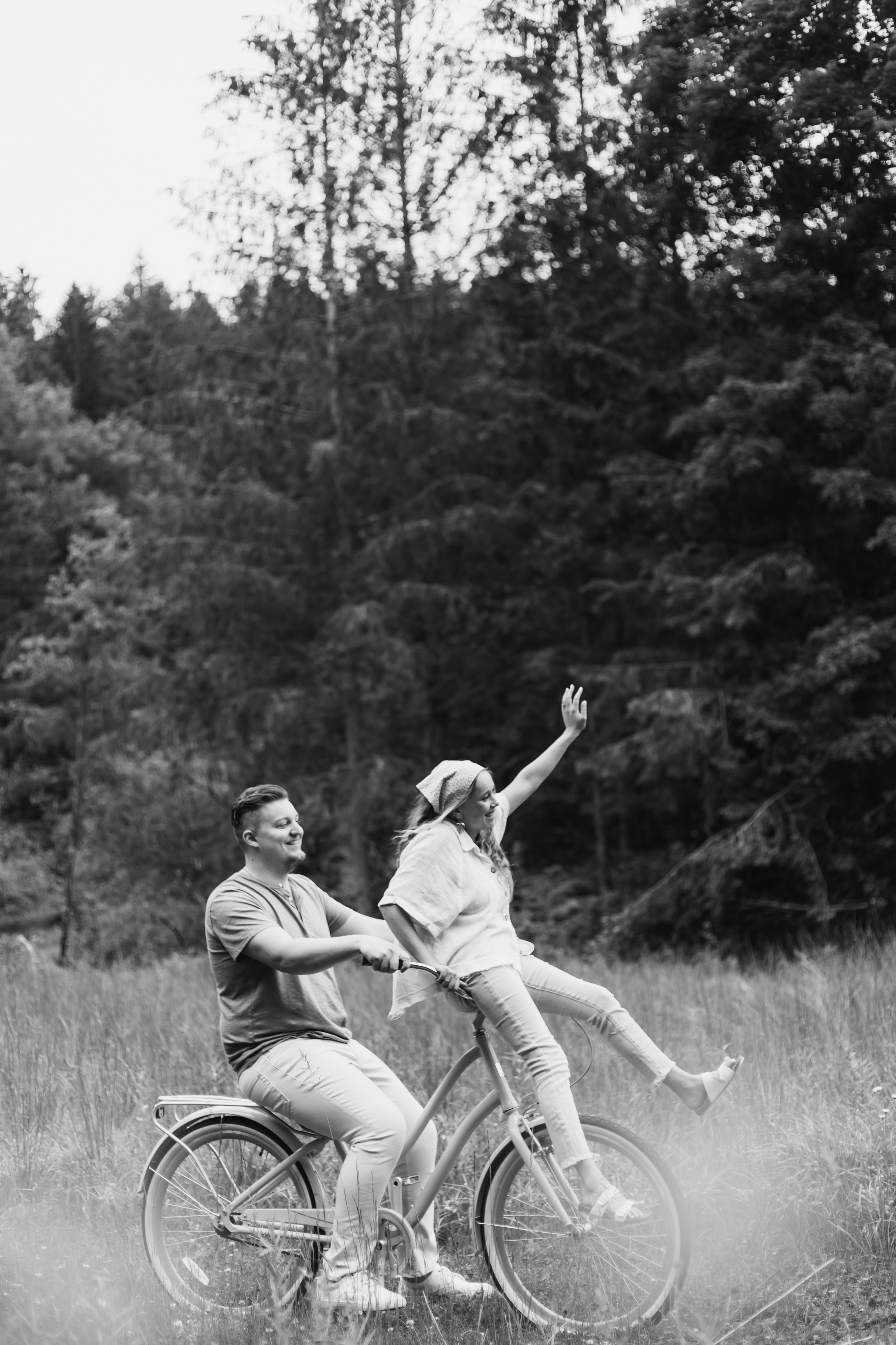 A black and white photo sequence showing a couple playfully interacting while sitting on a bicycle in a grassy field.