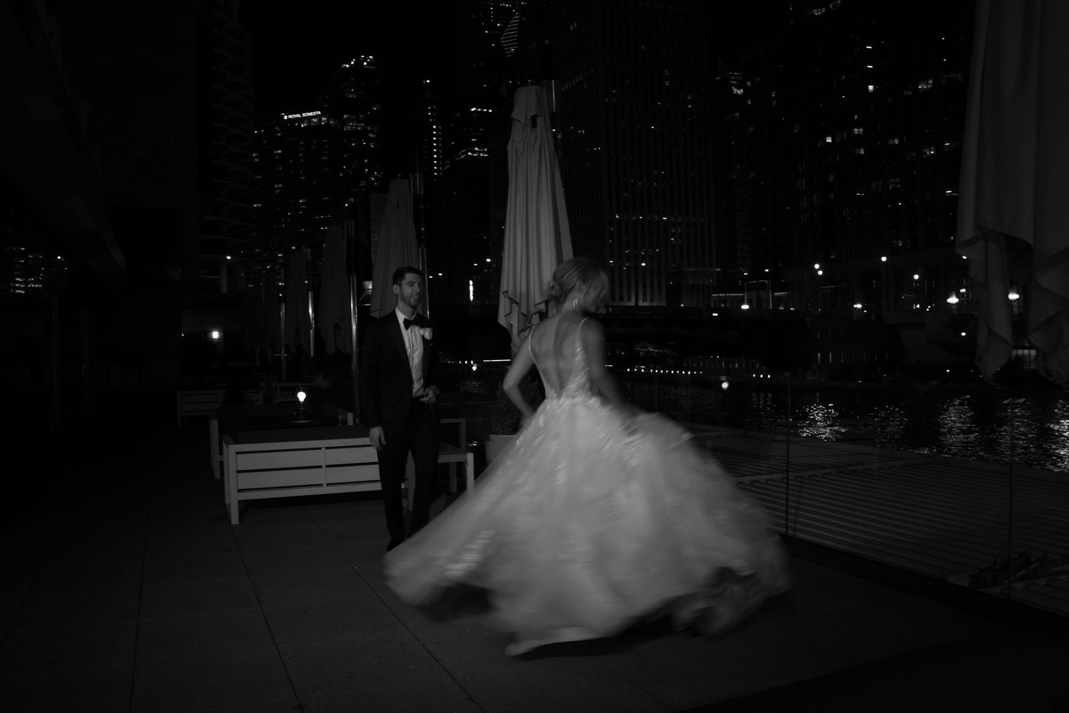 A wedding couple shares a romantic dance at night with city lights twinkling in the background.