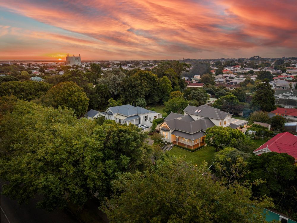 Aerial sunset view of a lush suburban neighborhood with tree-lined streets and residential homes under a vibrant orange sky.