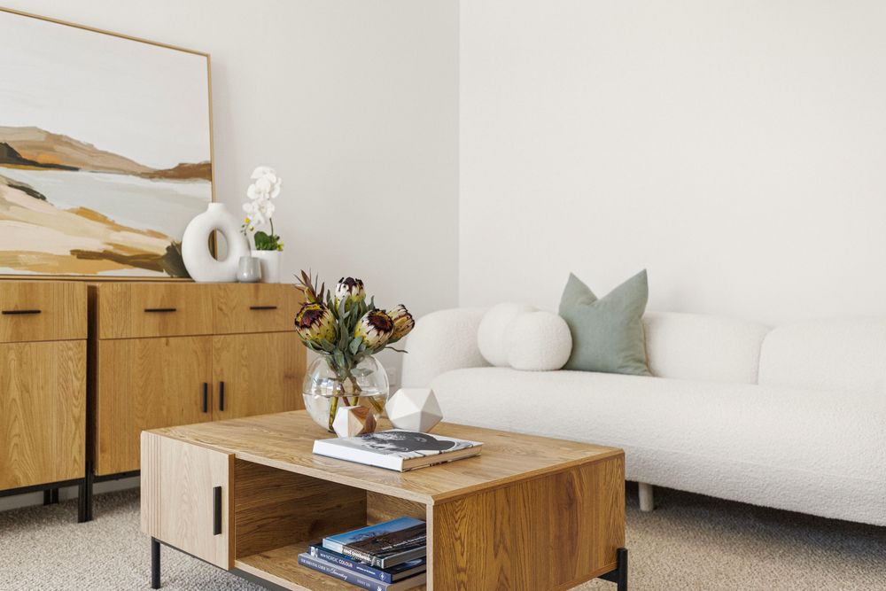 Modern living room with white sofa, wood coffee table, sideboard, and abstract art in neutral tones.