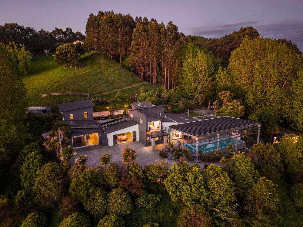 Aerial dusk view of a modern luxury home surrounded by lush green trees with panoramic countryside views.